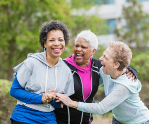 Three women laughing after finishing a run in a park
